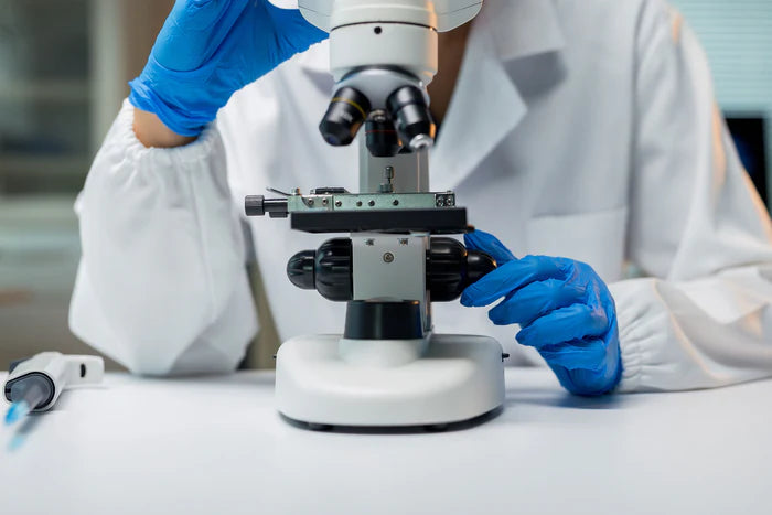 Scientist in a white lab coat and blue gloves using a microscope